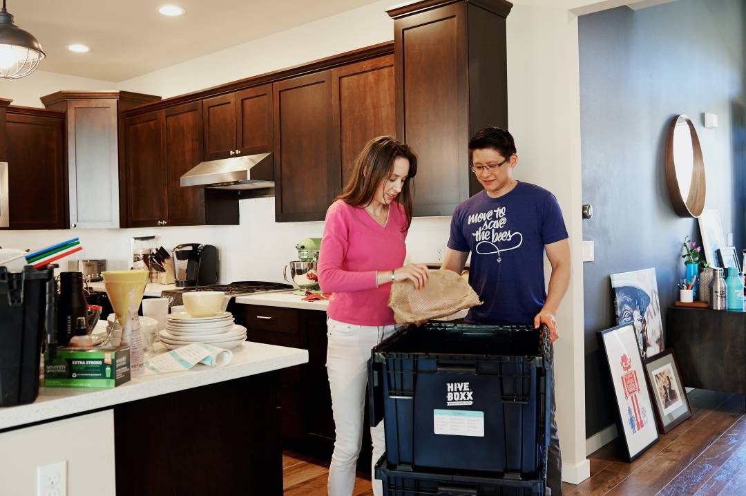Man And A Woman Packing Up A Kitchen Into Storage Boxes